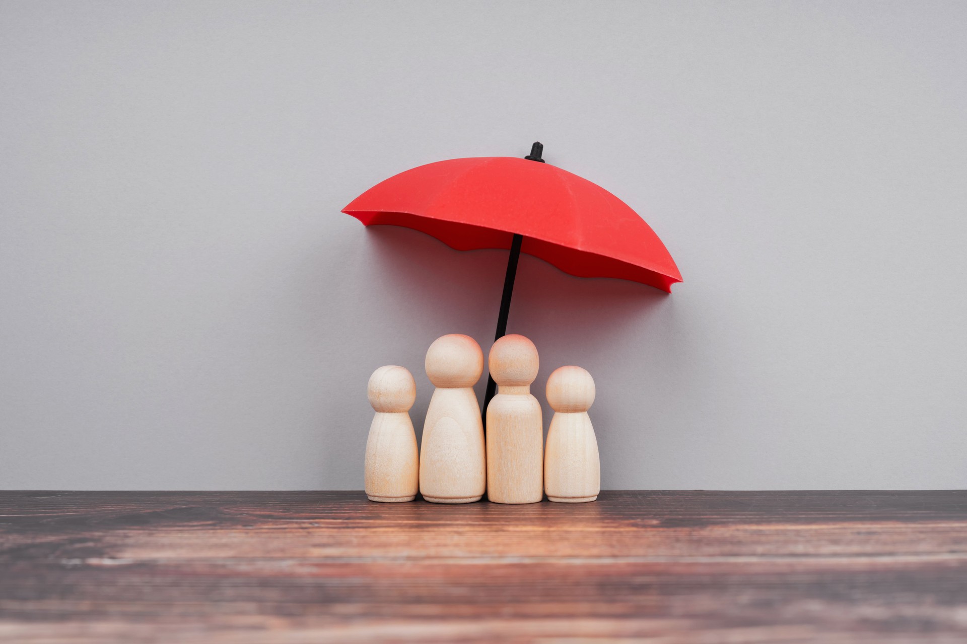 Family health and life insurance concept. Wooden people represent parent and children under a red umbrella. Family health and life insurance concept. Wooden people represent parent and children under a red umbrella.